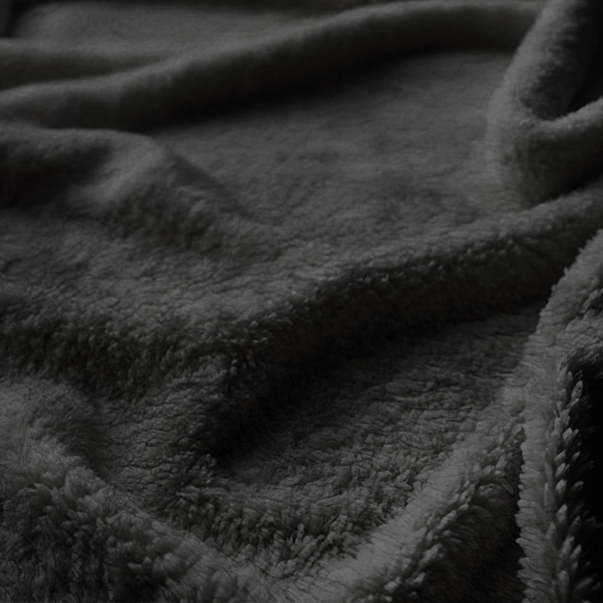 Close-up van de donkere, zachte en donzige stof van de Verduisterende Teddy Gordijn - Zwart, met zachte plooien en schaduwen.