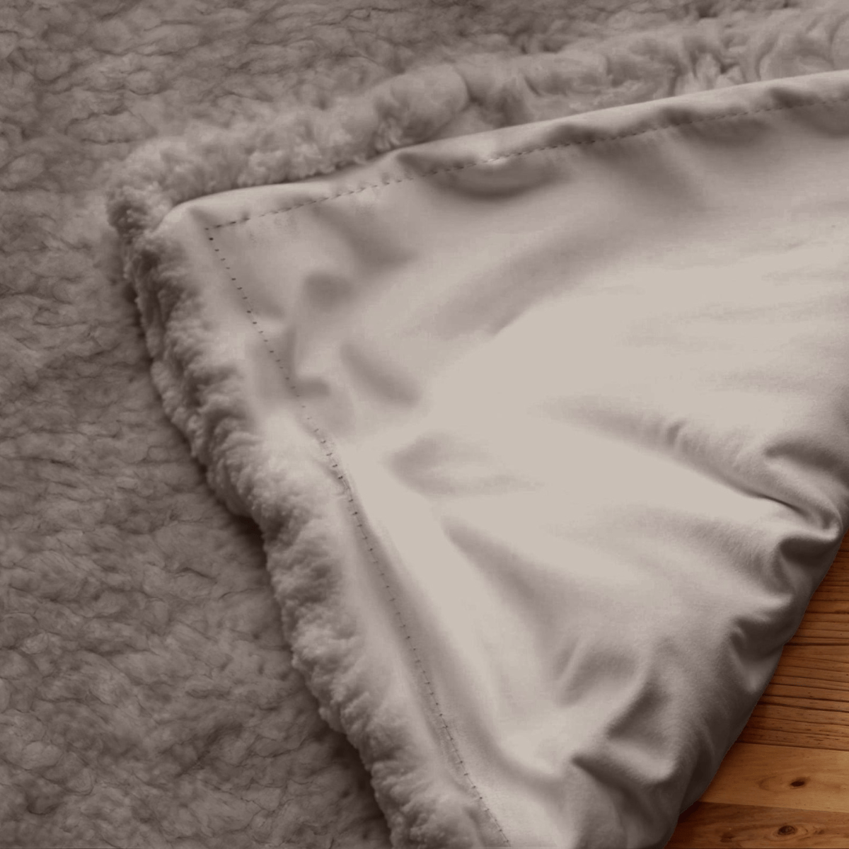 Een close-up van de Verduisterende Teddy Gordijn in taupe, met de zachte, pluizige teddystof stof omgedraaid in de hoek om de pluchen onderkant op een houten oppervlak te onthullen.