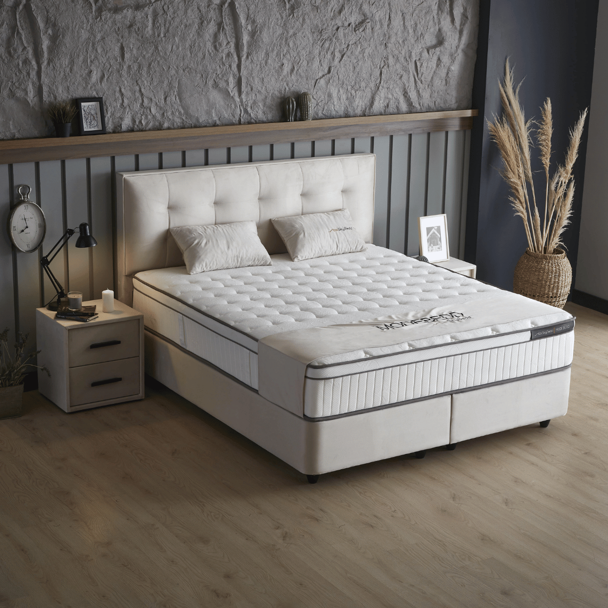 Een moderne slaapkamer met een luxe 3D-geweven stofbed, witte kussens, matras, Zelesta SkyBedd Odin - Beige Nachtkastje met lamp en klok, ingelijste foto's en een vaas met gedroogde planten.