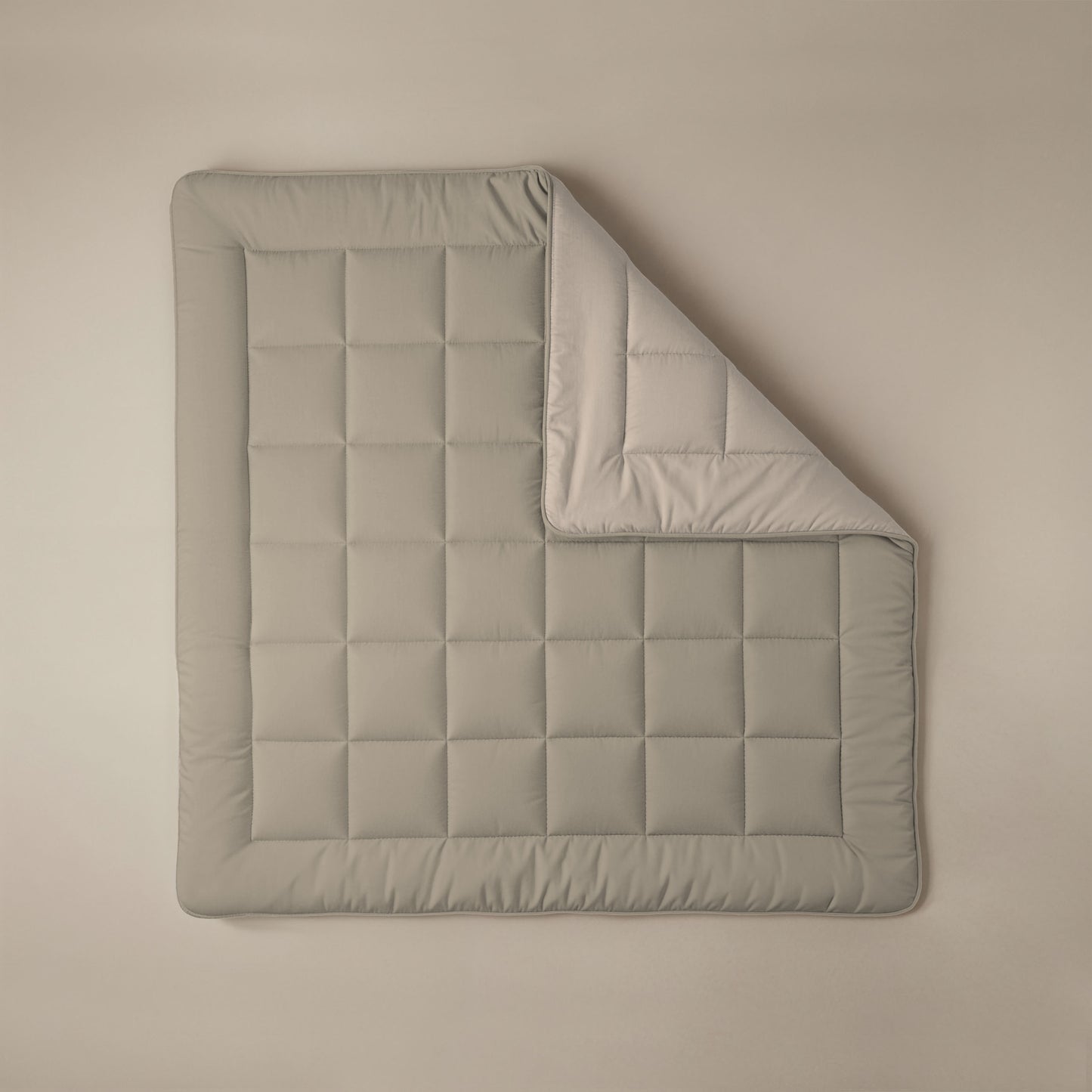 Een netjes opgemaakt Zelesta Comfort Duo Dekbed in taupe met een omgeslagen hoek, waardoor de champagnekleurige onderkant zichtbaar wordt, op een neutrale achtergrond - perfect als dekbed voor alle seizoenen.