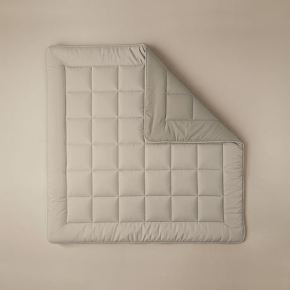 Het Zelesta Comfort Duo Dekbed in taupe & champagne, netjes gewatteerd met een omgeslagen hoek, staat op een beige achtergrond - perfect voor wie klassieke dekbedden en comfort het hele jaar door belangrijk vindt.