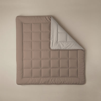 Het Zelesta Comfort Duo Dekbed - Terra & Zand is een bruine gewatteerde deken met een rasterpatroon, geïnspireerd op klassieke dekbedden. De deken is gedeeltelijk opgevouwen zodat de lichtgrijze onderkant zichtbaar wordt, en plat neergelegd voor een look het hele seizoen door.