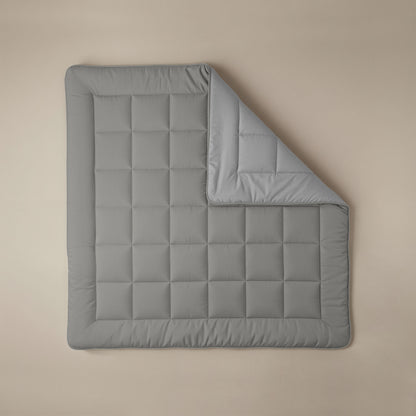 Het Zelesta Comfort Duo Dekbed in grijs en zachtgrijs ligt plat op een beige oppervlak, één hoek omgevouwen om beide kanten te laten zien, en combineert tijdloos comfort met moderne stijl.