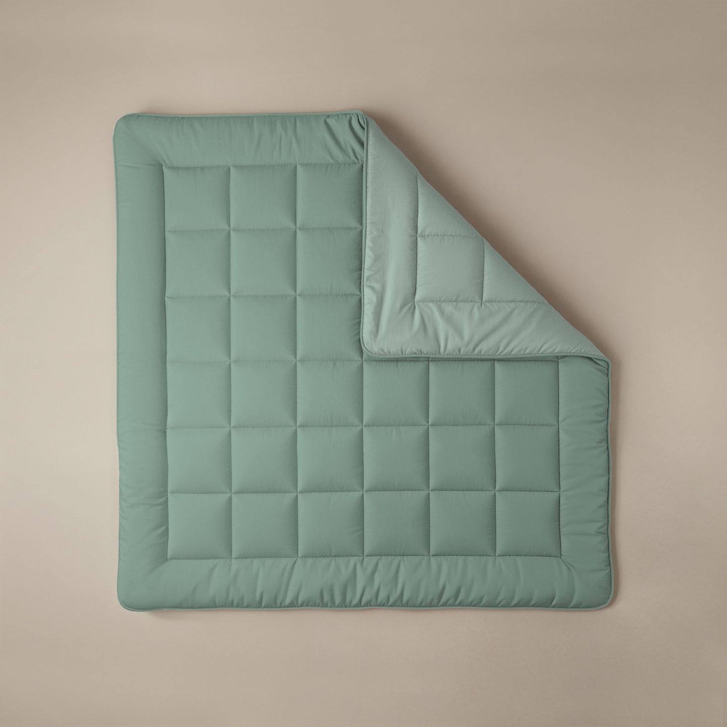 Het Zelesta Comfort Duo Dekbed in mintgroen & lichtgroen, een rechthoekig gewatteerd all-season dekbed, ligt plat op een beige ondergrond met één hoek netjes omgevouwen.