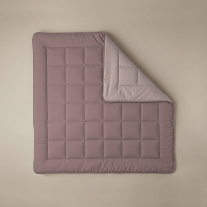 Het Zelesta Comfort Duo Dekbed in oudroze & lichtroze, met afgeronde hoeken en een doorgestikt dessin, wordt getoond op een beige oppervlak met een hoek omgevouwen om de lichtere kant te laten zien.