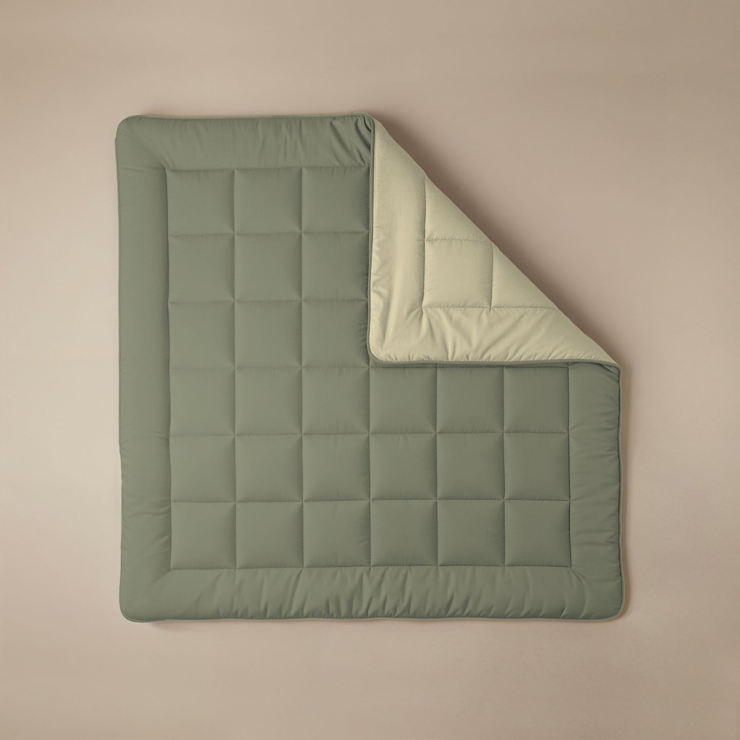 Het Zelesta Comfort Duo Dekbed in olijfgroen en crème is een gevouwen, vierkante, doorgestikte all-season deken met een groene bovenkant en lichtbeige onderkant, plat uitgelegd op een beige ondergrond.