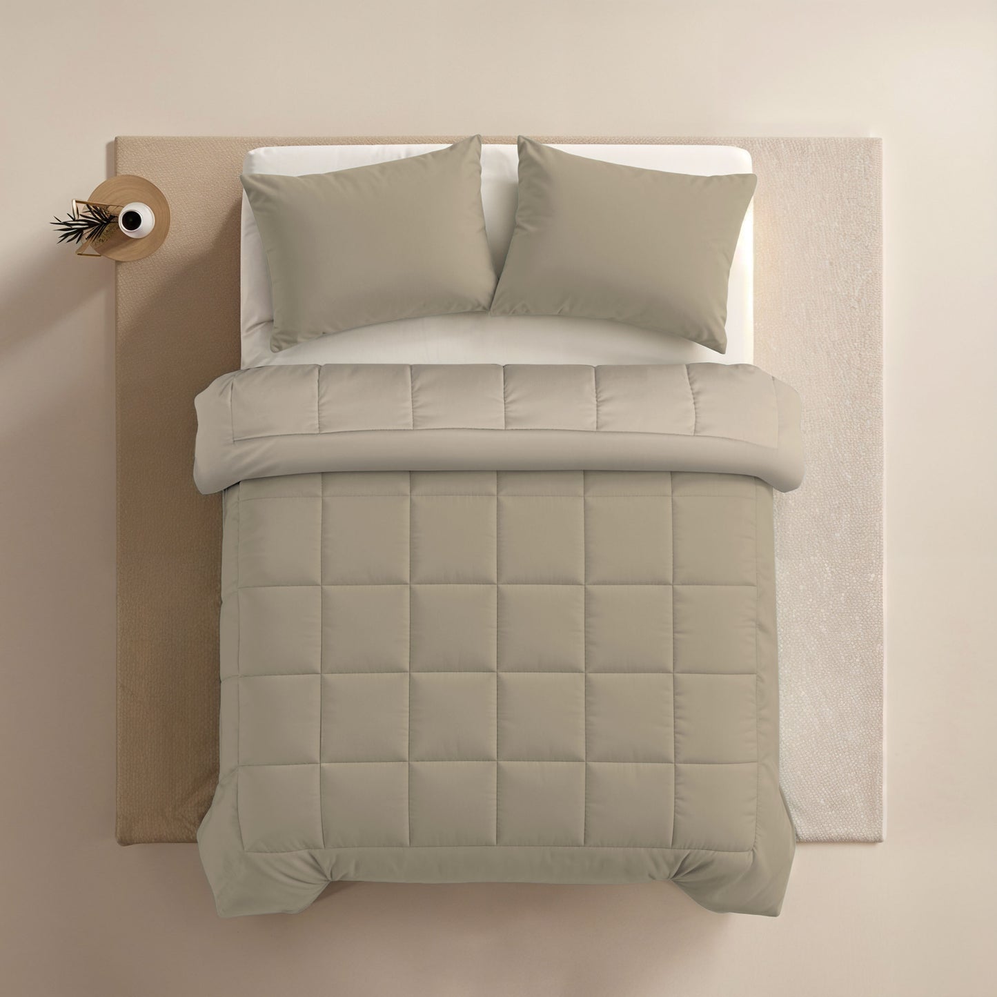 Het Zelesta Comfort Duo Dekbed in Taupe & Champagne staat op een netjes opgemaakt bed met twee kussens en een all-season dekbed, naast een bijzettafeltje met een kleine vaas met een tak.