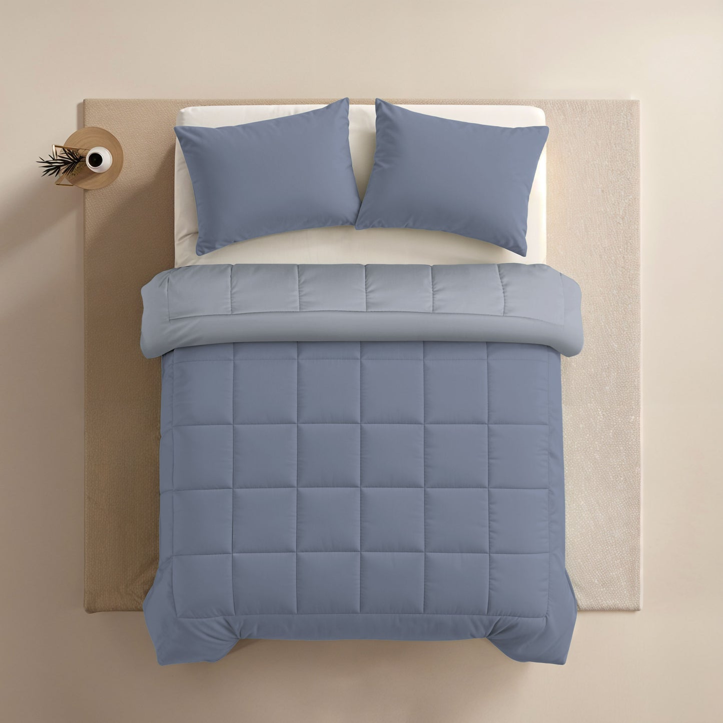 Bovenaanzicht van een netjes opgemaakt bed met blauw dekbed, Zelesta Comfort Duo Kussensloop - Ijsblauw, en een beige bijzettafel met een klein plantje.