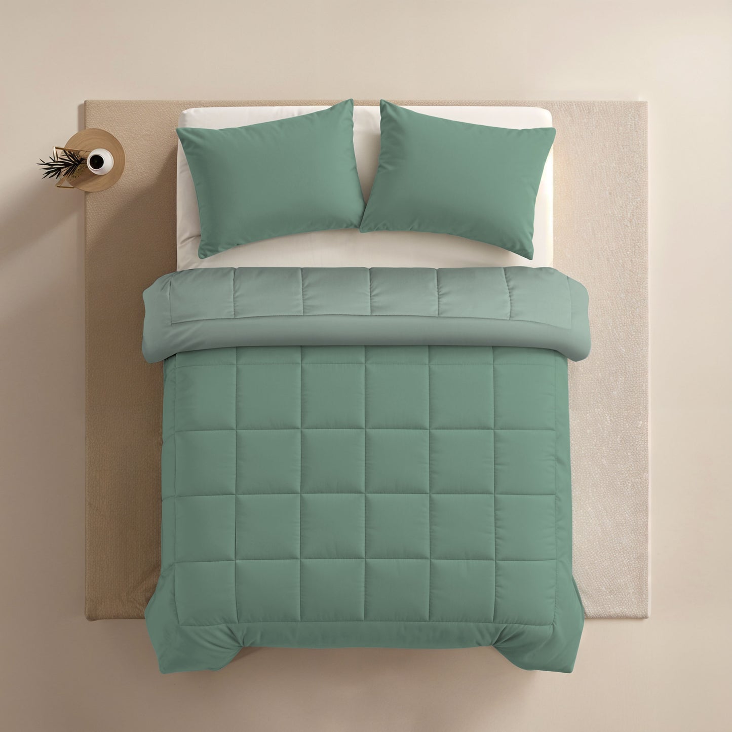 Een netjes opgemaakt bed met Zelesta Comfort Duo Dekbed in mint en lichtgroen, plus bijpassende groene kussens, van bovenaf gezien naast een kleine ronde tafel met een plant.