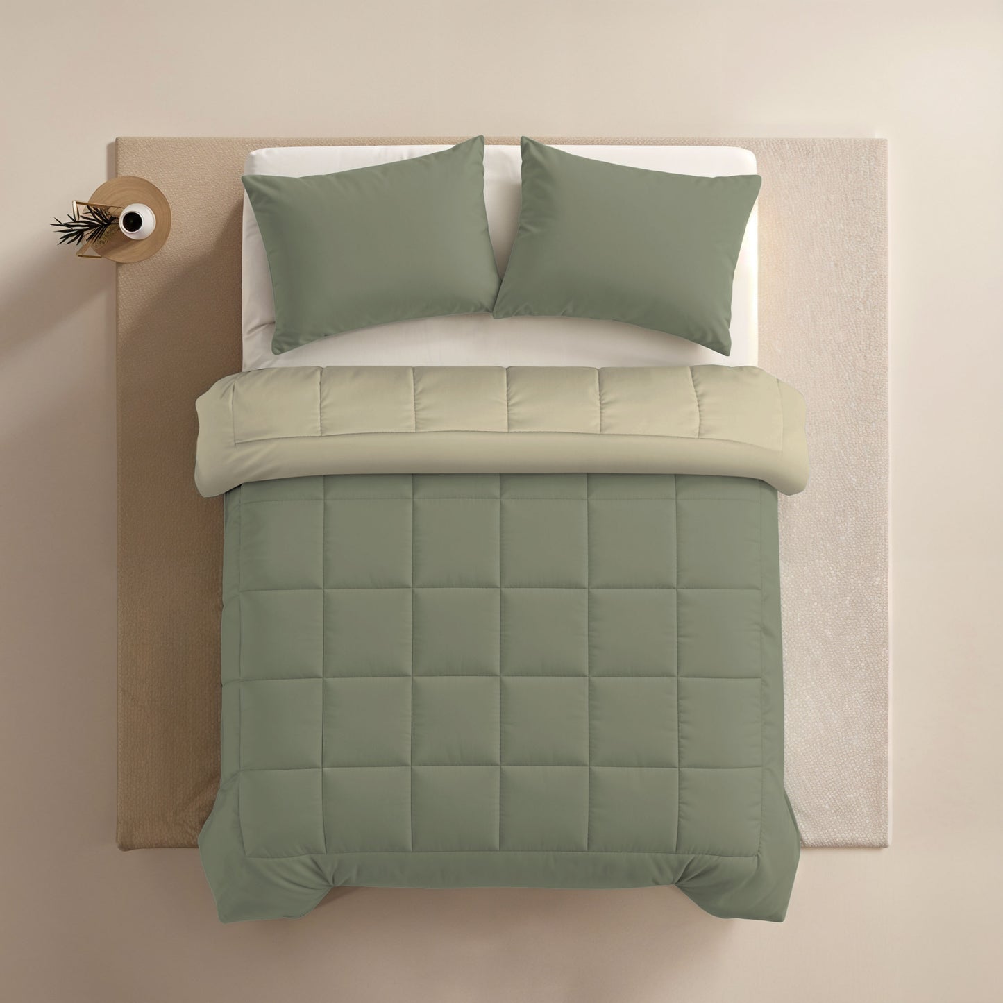 Bovenaanzicht van een netjes opgemaakt bed met saliegroene kussens, dekbed en beige laken naast een klein rond nachtkastje met een plant - ideaal om het Zelesta Comfort Duo Dekbed in Olijfgroen & Crème te accentueren.