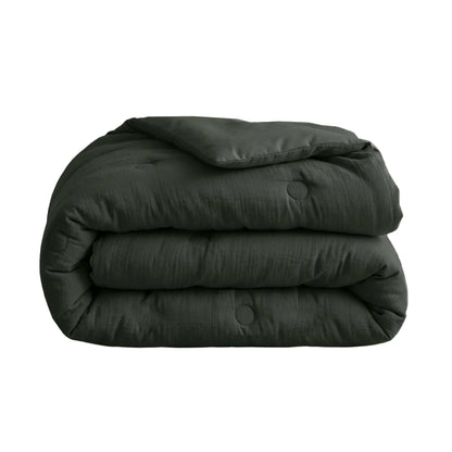 De Zelesta Japandibed Katoen Mousseline - Groen is een donkergroen, doorgestikt Japandi dekbed van dubbelgeweven katoen, netjes opgevouwen op een witte ondergrond.