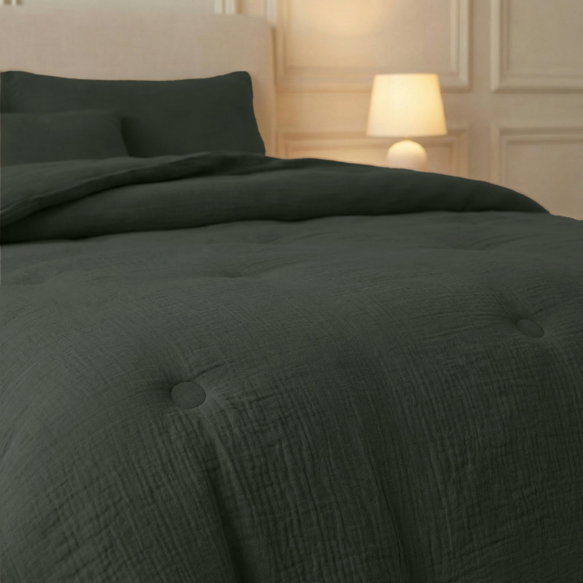 Een keurig opgemaakt bed met de Zelesta Japandibed Katoen Mousseline - Groen en kussens staat naast een brandend bedlampje, tegen een crèmekleurige muur met paneeldetails.