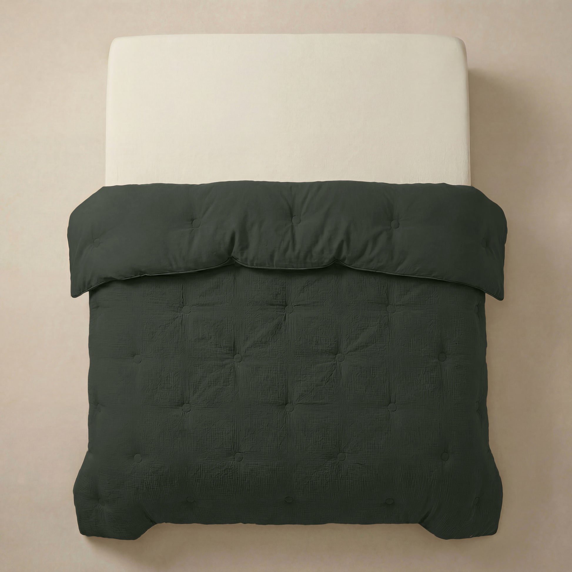 Een netjes opgemaakt bed met een crèmekleurig matras en het Zelesta Japandibed Katoen Mousseline - Green, een donkergroen getuft dekbed van dubbelgeweven katoen, van bovenaf gezien tegen een neutrale achtergrond.