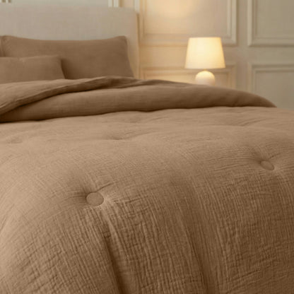 Een keurig opgemaakt bed met Zelesta Japandibed Katoen Mousseline - Bruin beddengoed en kussens, een getuft dekbed en een brandende tafellamp op een nachtkastje op de achtergrond.