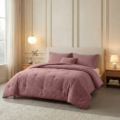 Een netjes opgemaakt bed met de Zelesta Japandibed Katoen Mousseline in Oudroze, met bijpassende kussens, staat tussen twee houten nachtkastjes met lampen in een zacht verlichte, neutraal getinte slaapkamer.