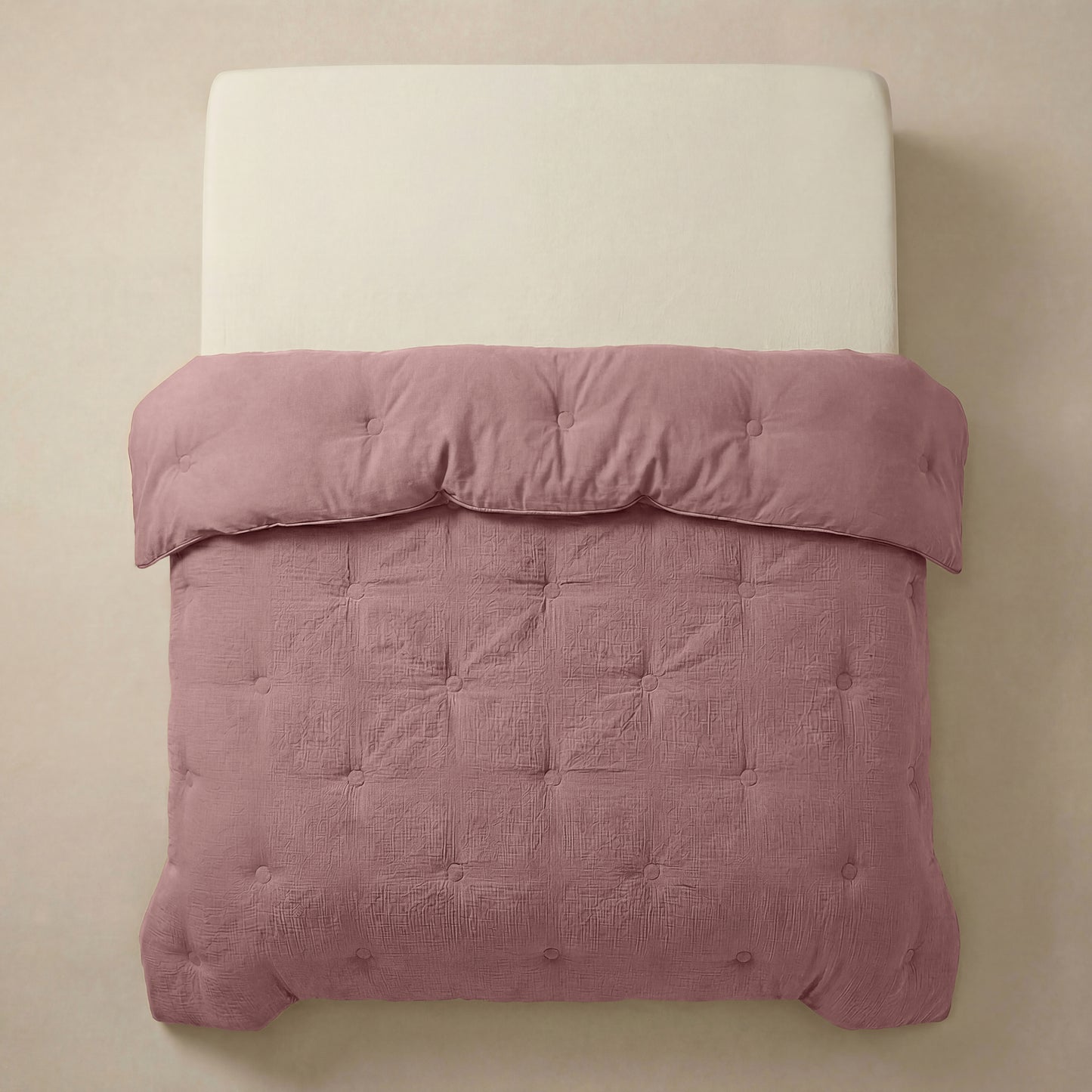 Een netjes opgemaakt bed met een crèmekleurig hoofdeinde en de Zelesta Japandibed Katoen Mousseline in Oudroze, getuft en zacht, tegen een neutrale muur.