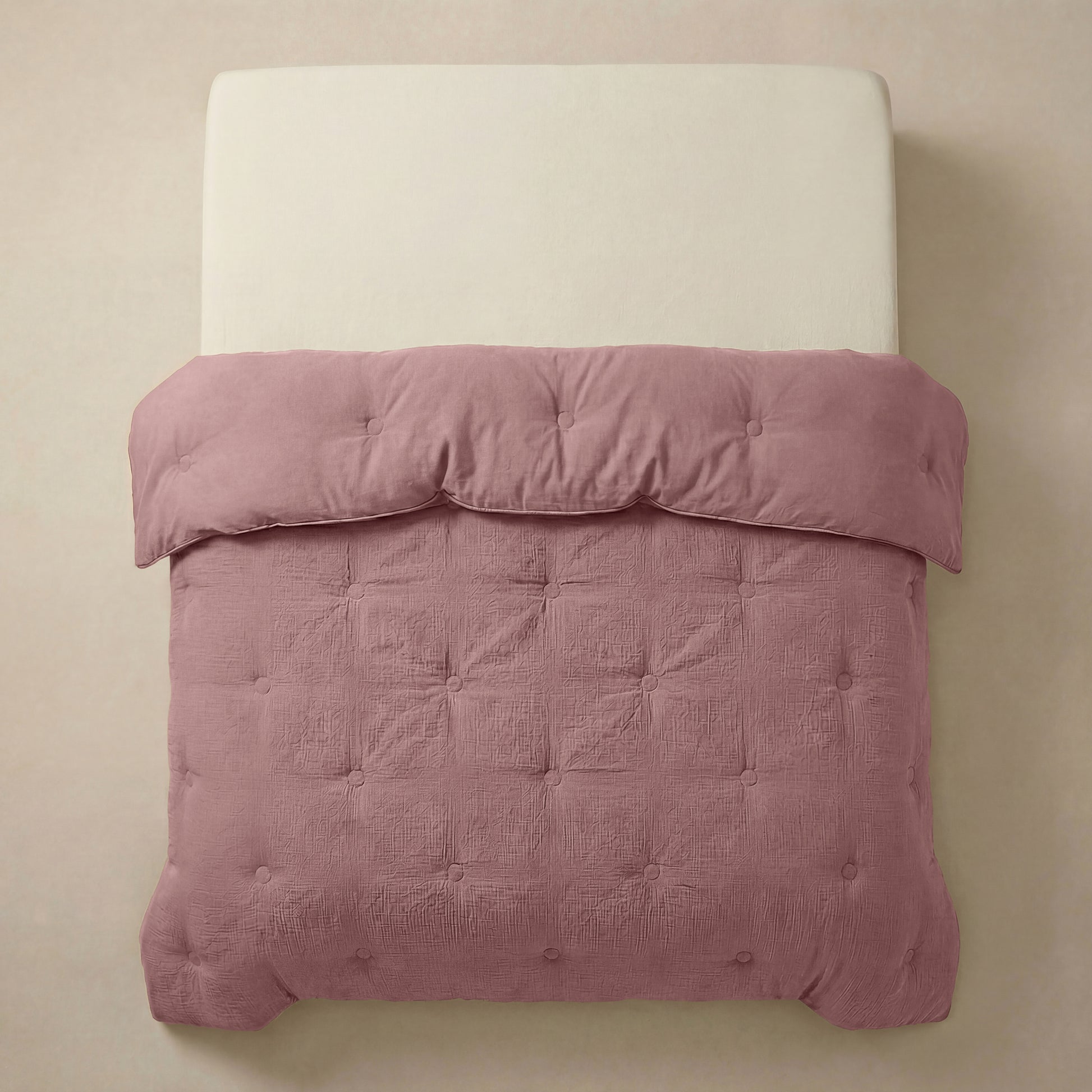 Een netjes opgemaakt bed met een crèmekleurig hoofdeinde en de Zelesta Japandibed Katoen Mousseline in Oudroze, getuft en zacht, tegen een neutrale muur.