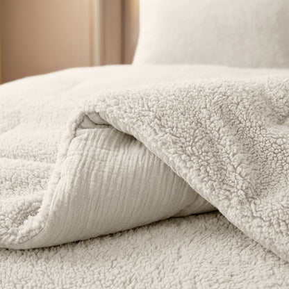 Een close-up van een netjes opgemaakt bed met het Zelesta Teddy Katoen Mousseline - Beige dekbed, bekend om zijn zachte, temperatuurregulerende comfort, met een gebroken witte sherpa deken gedeeltelijk teruggevouwen.