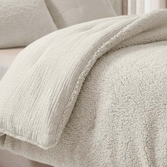 Close-up van het Zelesta Teddy Katoen Mousseline - Beige: een lichtkleurig dekbed met teddy-bovenzijde en zachte sherpa-onderkant, stijlvol in lagen met mousseline katoen en neutrale kussens; perfect temperatuurregulerend.
