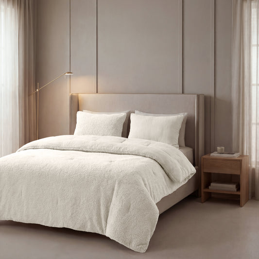 Een netjes opgemaakt bed met Zelesta Teddy Katoen Mousseline - Beige beddengoed staat tegen een beige wand, naast een houten nachtkastje en staande lamp, in een zacht verlichte slaapkamer.