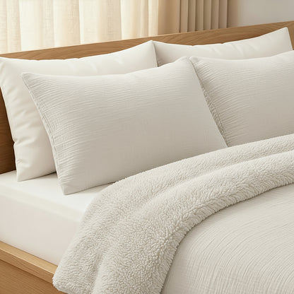 Op een netjes opgemaakt bed ligt de Zelesta Teddy Katoen Mousseline - Beige beddengoedset, met kussens met structuur, een glad mousseline katoenen laken en een donzig Teddy dekbed in een houten frame bij beige gordijnen.