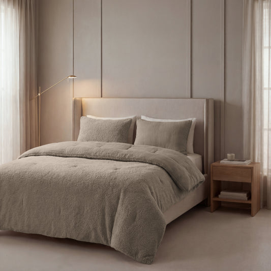 Een moderne, neutraal getinte slaapkamer met een groot gestoffeerd bed met beddengoed van Zelesta Teddy Katoen Mousseline - Taupe, een houten nachtkastje, minimalistische inrichting, natuurlijk licht en een zacht gloeiende vloerlamp.