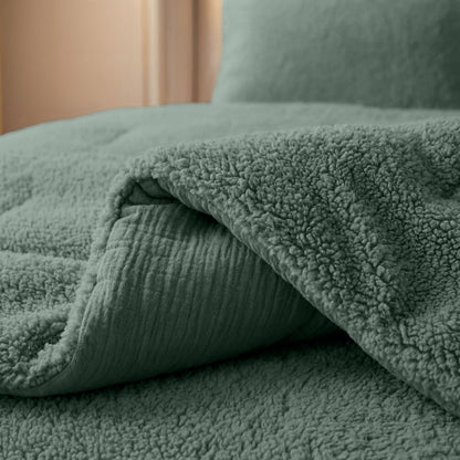 Close-up van het Zelesta Teddy Katoen Mousseline - Groen dekbed en kussen op een bed in zachte verlichting, met de knusse warmte en de getextureerde look van sherpa fleece.