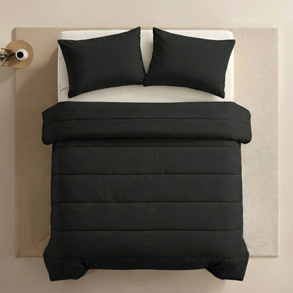 Een netjes opgemaakt bed met het Zelesta Comfort Uni Dekbed - Zwart en bijpassende zwarte kussens, op een beige vloerkleed naast een ronde bijzettafel met een vaas.