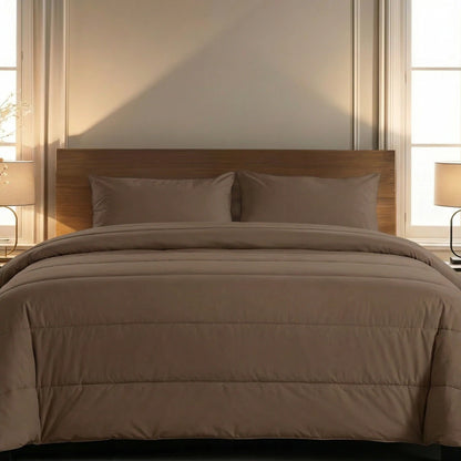 Een keurig opgemaakt bed met het Zelesta Comfort Uni Dekbed - Mokka en twee kussens, geflankeerd door bijpassende lampen op nachtkastjes, staat tegen een muur met twee ramen - ideaal voor een opfrisbeurt van de slaapkamer het hele seizoen door.