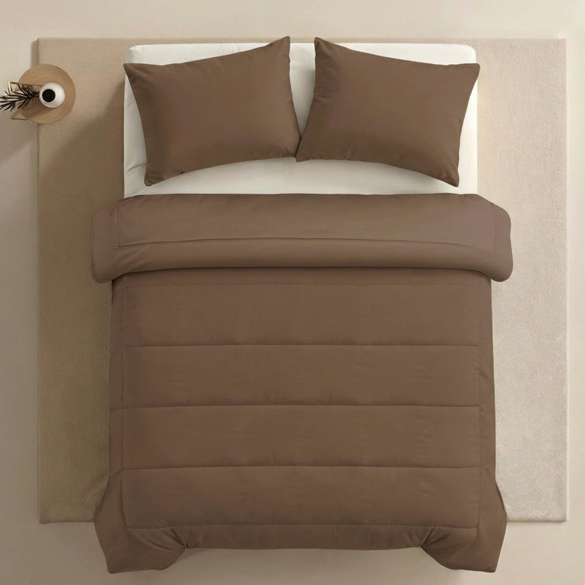 Een keurig opgemaakt bed met bruin Zelesta Comfort Uni Dekbed - Mokka en twee bijpassende kussens staat op een beige vloerkleed, naast een klein rond bijzettafeltje met een decoratief voorwerp.