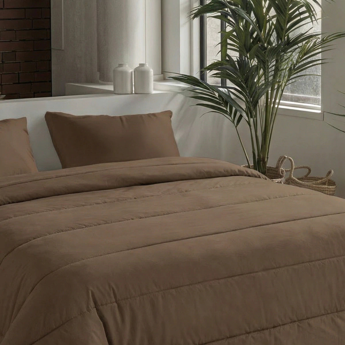 Een netjes opgemaakt bed met het Zelesta Comfort Uni Dekbed - Mokka, twee kussens en bruin beddengoed staat bij een potplant en een raam. Op een plank op de achtergrond staan twee witte potten.
