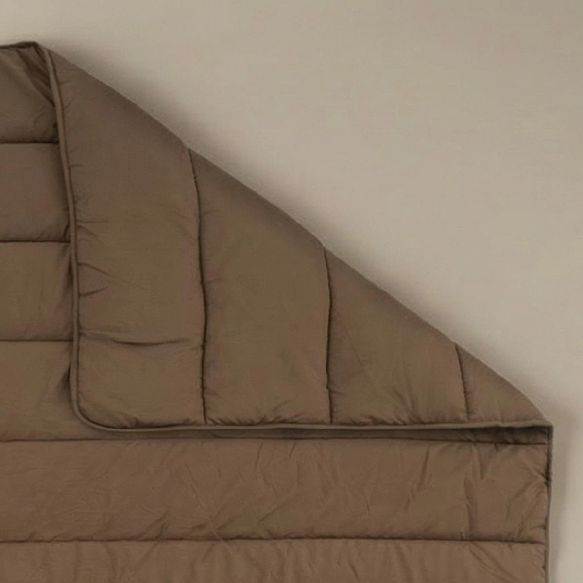 Het Zelesta Comfort Uni Dekbed - Mokka, geïnspireerd op klassieke dekbedden, wordt rechtsboven gedeeltelijk opgevouwen getoond tegen een effen achtergrond.