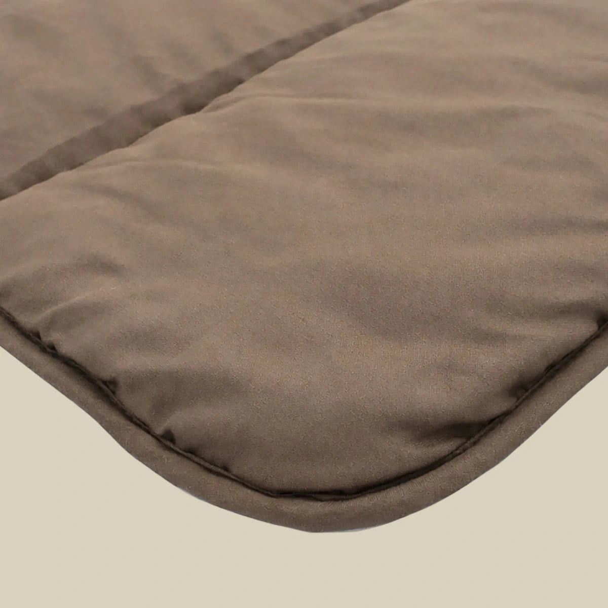 Close-up van het Zelesta Comfort Uni Dekbed - Mokka, een favoriet voor alle seizoenen, met de bruine gewatteerde stof, zachte textuur en afgeronde gestikte hoek tegen een eenvoudige achtergrond.