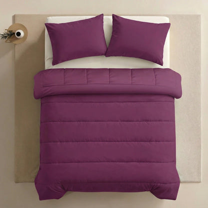 Een netjes opgemaakt bed met het Zelesta Comfort Uni Dekbed in bordeaux met twee bijpassende kussens, op een beige ondergrond naast een klein rond bijzettafeltje met een enkele vaas.