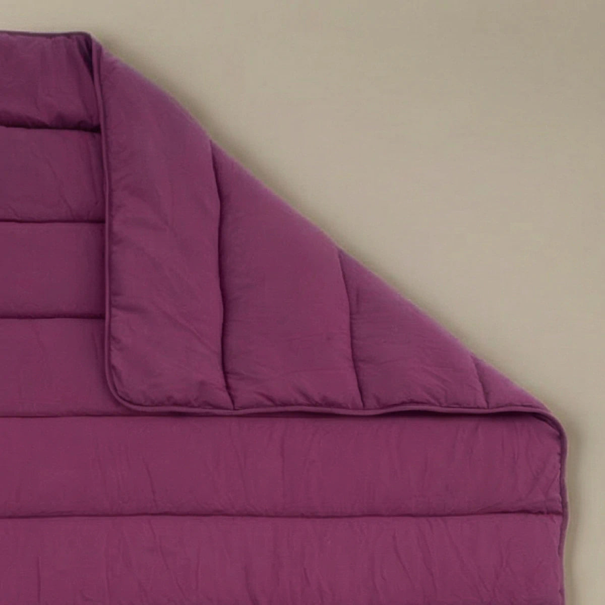 Het Zelesta Comfort Uni Dekbed in bordeaux, geïnspireerd op klassieke dekbedden, wordt plat op een beige ondergrond getoond, met één hoek netjes omgevouwen.