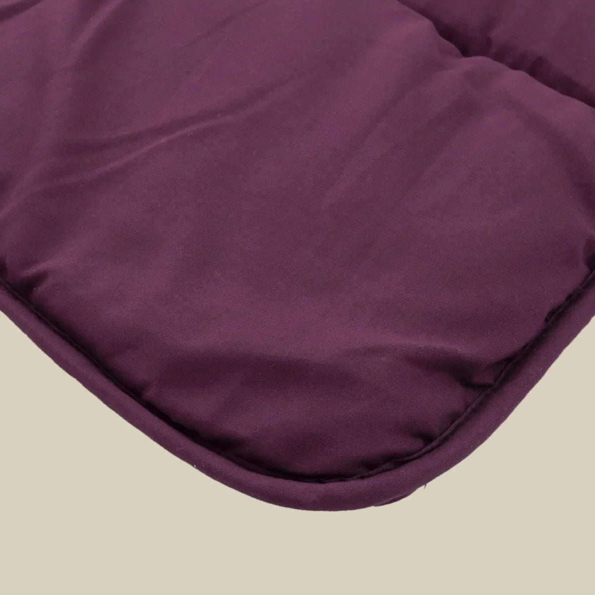 Close-up van een gevoerde, kastanjebruine stoffen hoek met gestikte randen van het Zelesta Comfort Uni Dekbed - Bordeaux, tegen een effen beige achtergrond.
