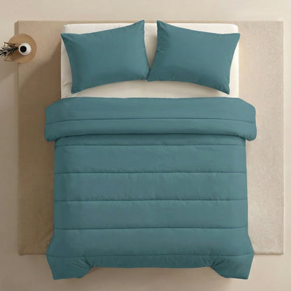 Een keurig opgemaakt bed met het Zelesta Comfort Uni Dekbed in zeegroen en twee bijpassende kussens, geplaatst op een crèmekleurig vloerkleed naast een klein rond nachtkastje met een vaas.
