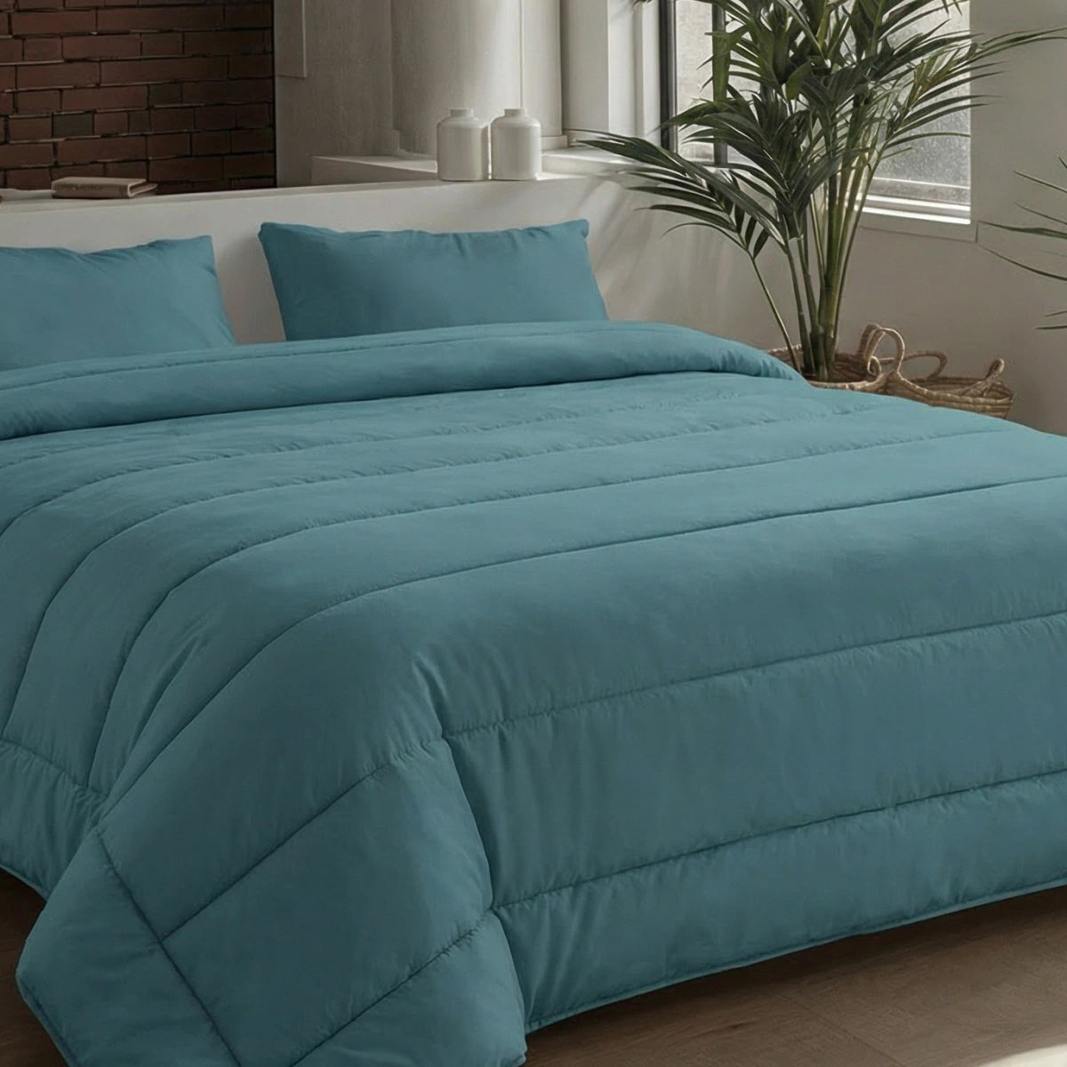 Een netjes opgemaakt bed met een groenblauw dekbed en twee bijpassende kussens, in een moderne slaapkamer met een potplant en een groot raam, is voorzien van het Zelesta Comfort Uni Dekbed - Zeegroen voor perfect comfort het hele seizoen door.