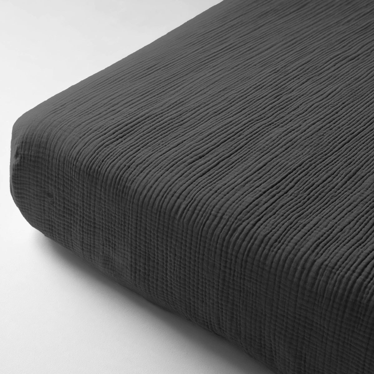 Close-up van het Mousseline Hoeslaken - Antraciet, een donkergrijs hoeslaken met een subtiel structuurpatroon, gemaakt van dubbel geweven perkal voor meer comfort en duurzaamheid.