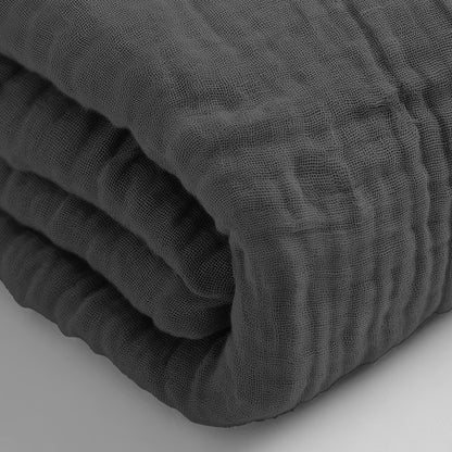 Een close-up van de Mousseline Hoeslaken - Antraciet toont het donkergrijze, gestructureerde, gekreukelde oppervlak van mousseline katoen.