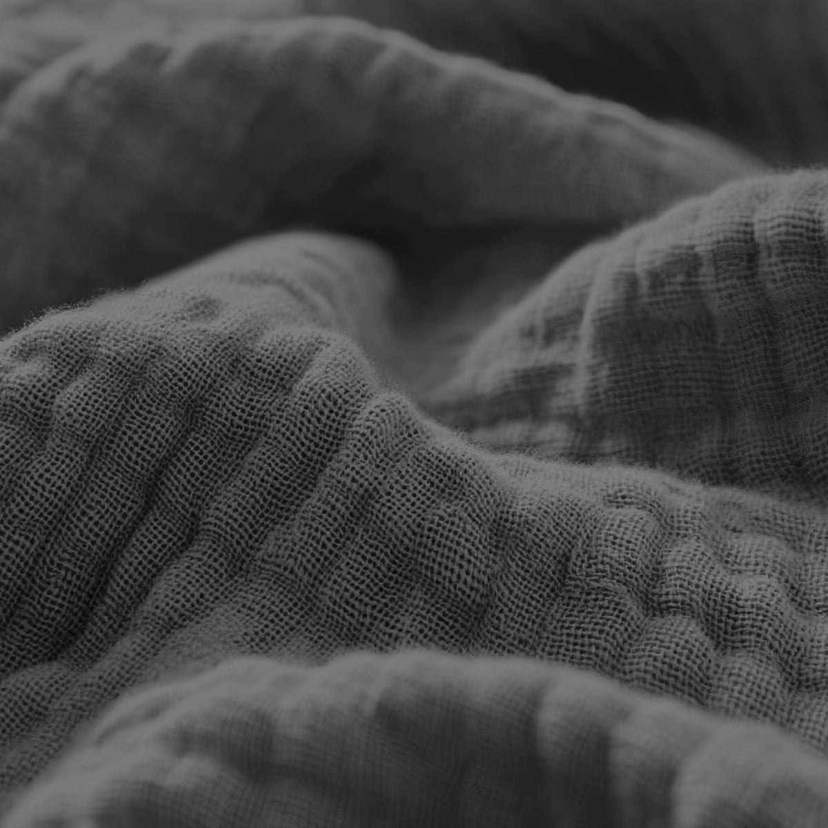 Close-up van het gestructureerde, gerimpelde oppervlak van de Mousseline Hoeslaken - Antraciet, met de nadruk op het zachte, golvende gevoel in grijstinten, geïnspireerd op Japandi design en doet denken aan dubbelgeweven perkal.