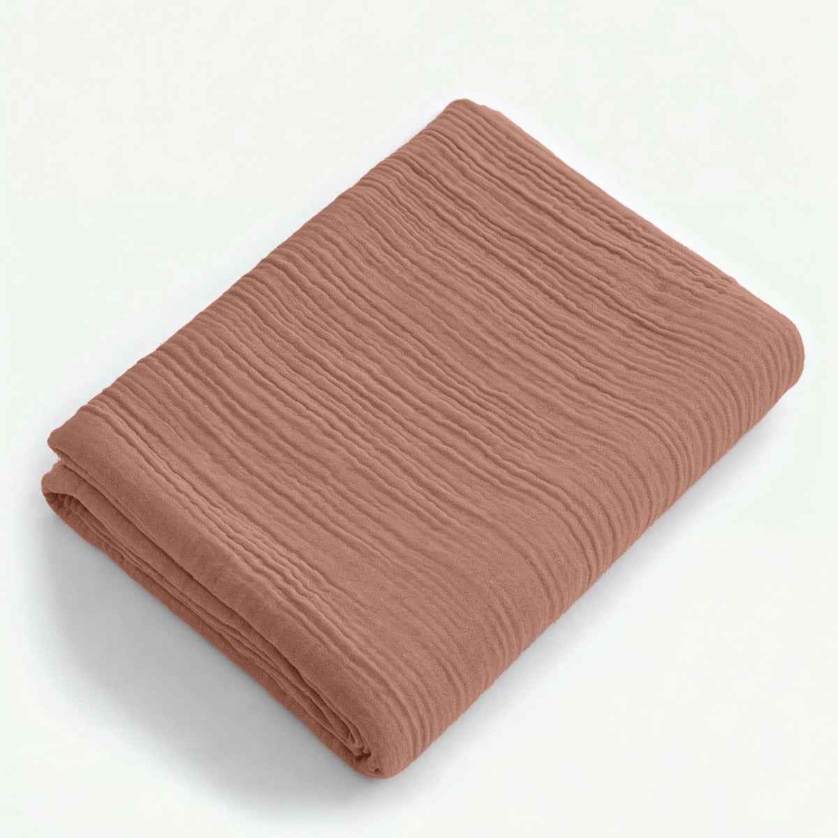 De Mousseline Hoeslaken - Dusty-Rose, een gevouwen hoeslaken van mousseline met textuur in lichtbruin, wordt getoond op een effen witte achtergrond - ideaal voor iedereen die op zoek is naar ademend beddengoed.