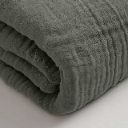 Een gevouwen, grijsgroene Mousseline Hoeslaken staat op een wit oppervlak, waardoor het ideaal is als beddengoed voor elke Japans geïnspireerde ruimte.