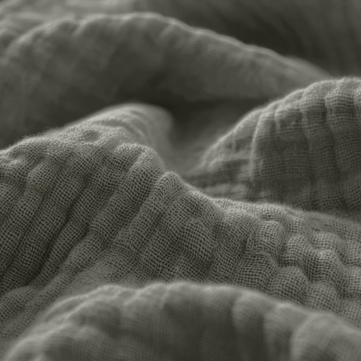 Close-up van verfrommeld, gestructureerd Mousseline Hoeslaken - Grijsgroen met zichtbare weefdraden, ideaal voor ademend beddengoed of een Japandi stijl hoeslaken.