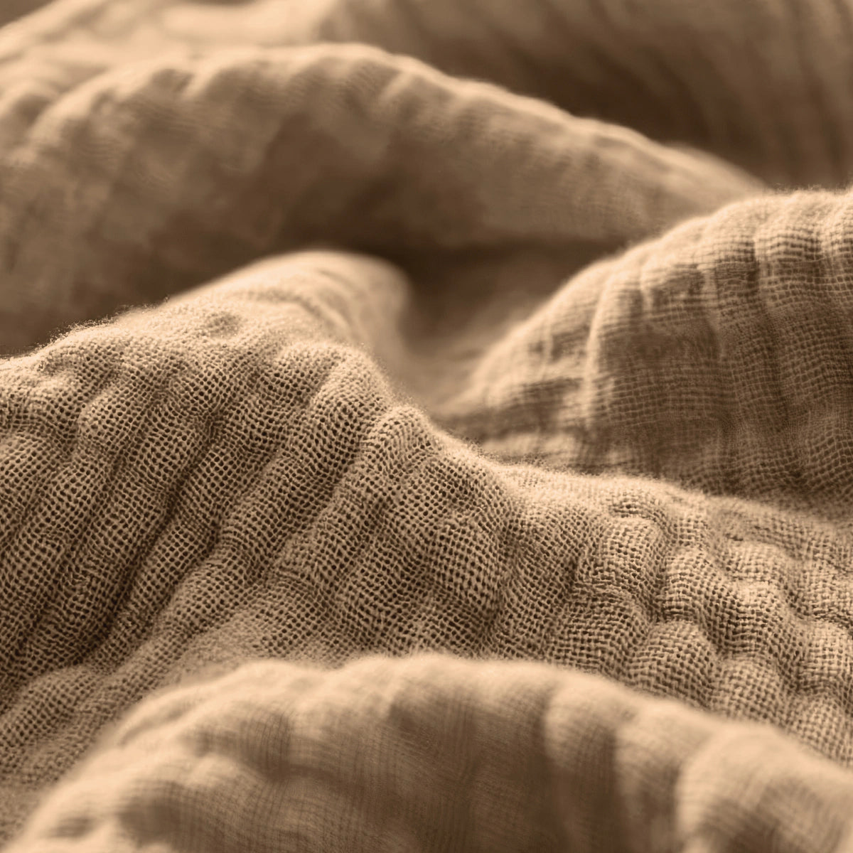 Close-up van taupe Mousseline Hoeslaken stof, met een gestructureerd, golvend oppervlak en zichtbare weving - ideaal voor ademend beddengoed of als Japandi-stijl hoeslaken.