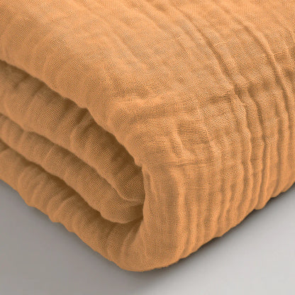 Een close-up van het Mousseline Hoeslaken - Terra, een gevouwen hoeslaken van lichtbruin katoen met textuur op een licht oppervlak, dat de ademende stof benadrukt - perfect voor serene slaapkamers in Japanse stijl.