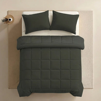 Een keurig opgemaakt bed met donkergroen superzacht katoen beddengoed en twee Zelesta Pure Uni kussenslopen (Olijfzwart) op een licht vloerkleed, van bovenaf gezien. Een klein bijzettafeltje met een vaas en plant staat naast het bed.