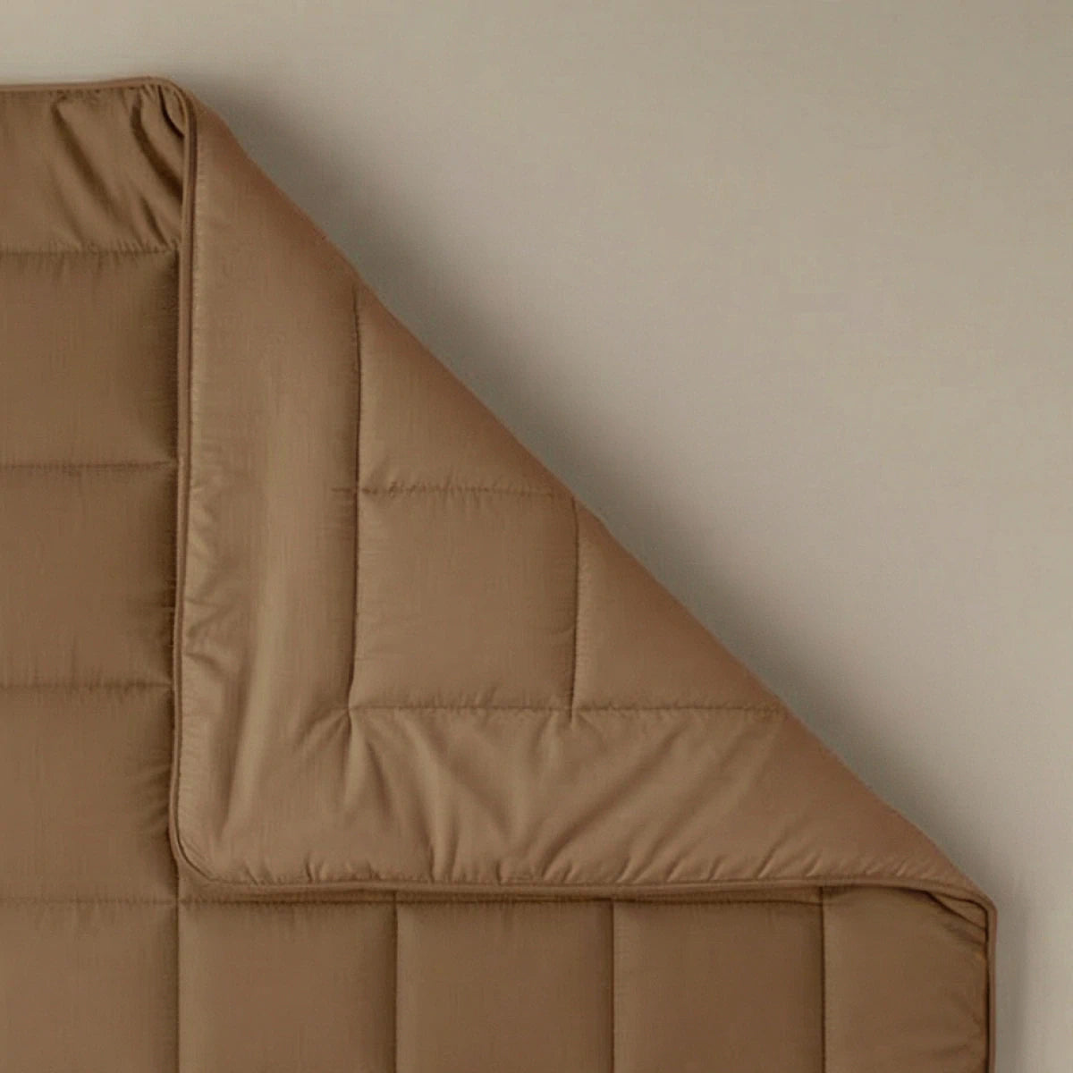 Een close-up van het Zelesta Pure Uni Dekbed in cacao bruin, met een doorgestikt dessin netjes gevouwen op een beige oppervlak voor ademend slaapcomfort.