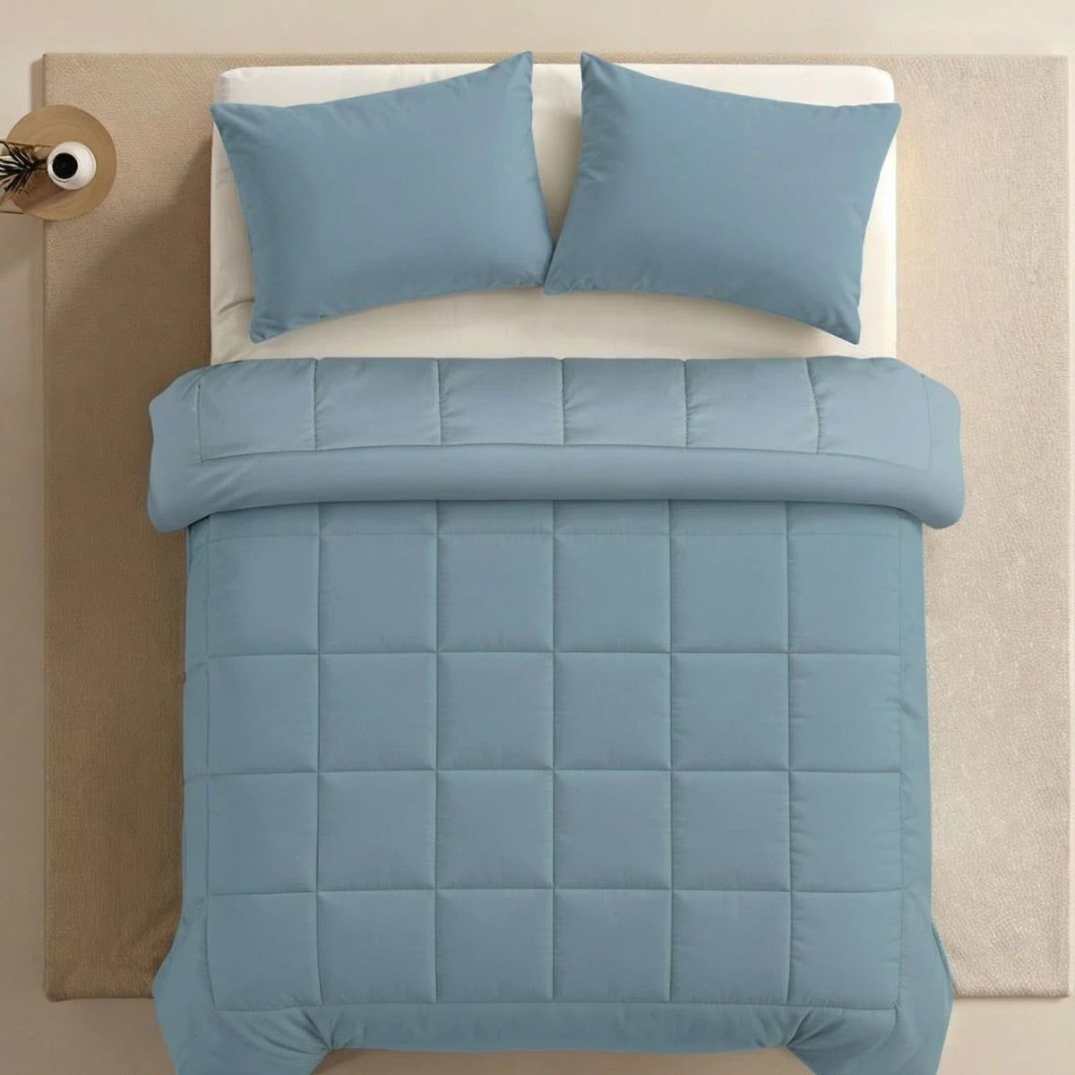 Een netjes opgemaakt bed met het Zelesta Pure Uni Dekbed in sereen blauw, gecombineerd met bijpassende kussens op een crèmekleurig vloerkleed en frame, benadrukt het ultieme slaapcomfort dankzij dit luxe katoenen dekbed.