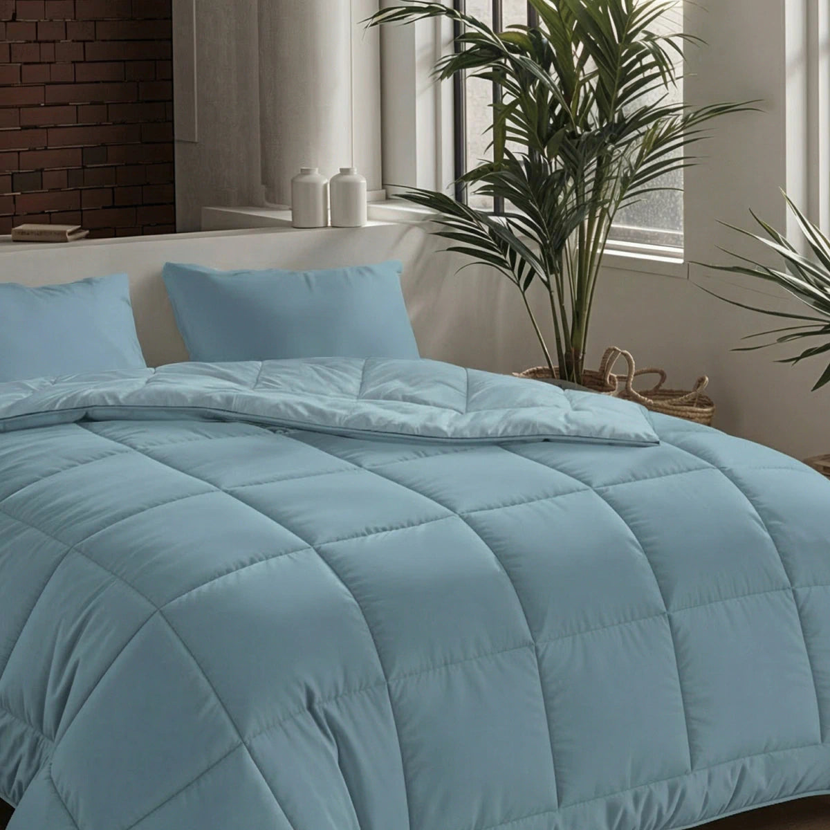 Een keurig opgemaakt bed met het Zelesta Pure Uni Dekbed in sereen blauw en kussens staat bij grote ramen en kamerplanten in een moderne slaapkamer en zorgt voor een ademend slaapcomfort.